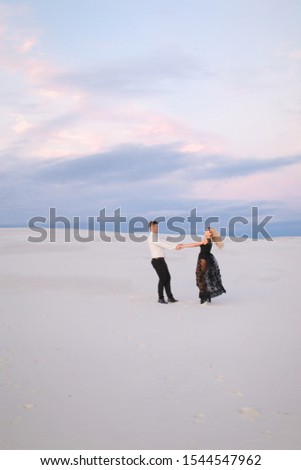 Man and woman wearing black dress walking in snowed white steppe. Concept of relationaship nad winter photo session.