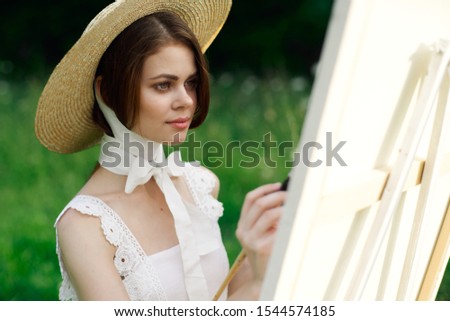 young woman in a summer white dress in a forest glade in a straw hat draws