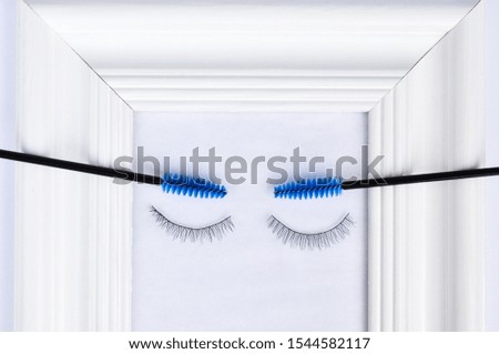 Beautiful eyelashes and eyebrows concept: white photo frame decorated with eyelash extensions and tools and gift on white background.