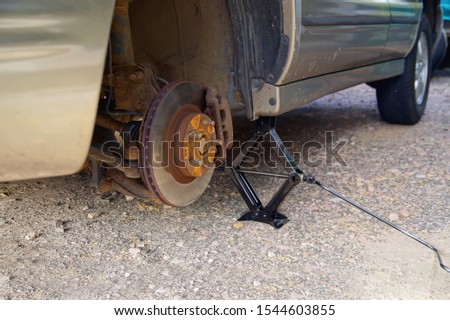 rusty brake disc and car jack on the concrete floor. Mechanical and season, tire concept. Replacement of winter and summer tires. Process of maintenance autumn. Replacing wheels in a passenger car. 