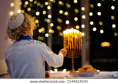 Kids celebrating Hanukkah. Jewish festival of lights. Children lighting candles on traditional menorah. Boy in kippah with dreidel and Sufganiyah doughnut. Israel holiday.