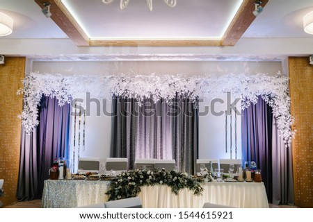 Festive table, arch decorated with winter composition of with fur tree branches in the banquet hall. Table newlyweds in the banquet area on party. Christmas winter wedding. Event.