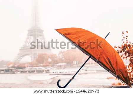 Bright orange umbrella on a rainy autumn foggy day in Paris against the background of the Eiffel tower