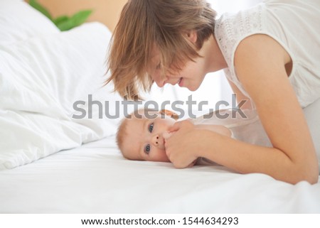 Mom and baby in white pajamas. They are lying in bed and hugging. Tender care and joy of motherhood. The boy and his parents woke up in the morning.
