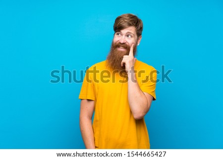 Redhead man with long beard over isolated blue background thinking an idea while looking up
