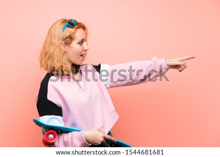 Young skater woman over isolated pink background pointing finger to the side