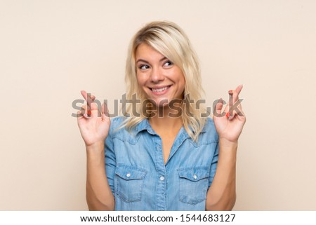 Young blonde woman over isolated background with fingers crossing