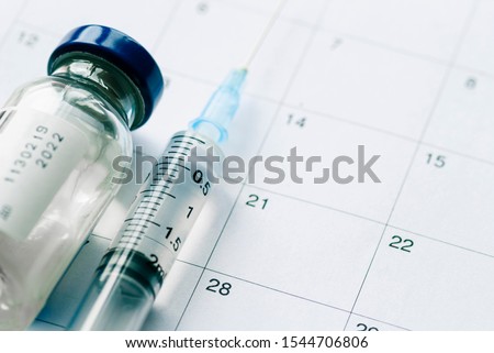 The vial with vaccine and syringe on calendar background, as a concept of vaccination season and date. Viewed from above with copy space Royalty-Free Stock Photo #1544706806
