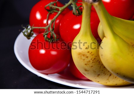 Bananas and Tomato together placed on a white plate against a black background.