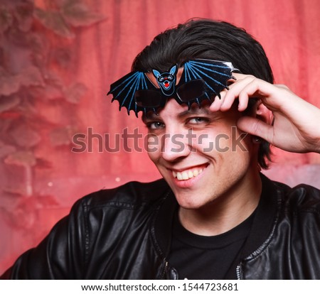 a young caucasian guy in the funny glasses in the form of a black bat at Halloween party smiling with open mouth.