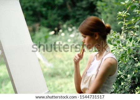 young woman outdoors paints an easel picture