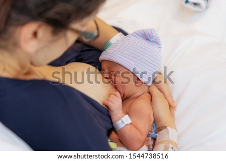 newborn baby in hospital after just being born, mother holding him and breastfeeding in hospital bed mother is dressed in blue night gown Royalty-Free Stock Photo #1544738516