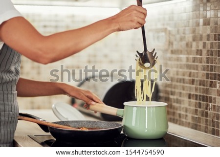 Cropped picture of mixed race woman in apron standing next to stove and making spaghetti.