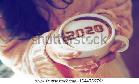 Number 2020 on frothy surface of cappuccino served in white cup holding by female hands with French nail polish. Food art creative concept for active days in New Year 2020. (close up, selective focus) Royalty-Free Stock Photo #1544755766