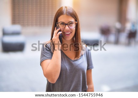 Young beautiful woman smiling happy and confident. Standing with smile on face talking by the smartphone at town street