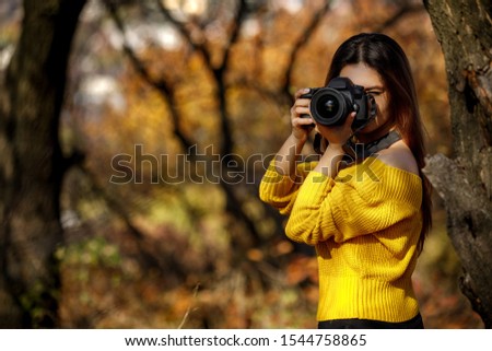 woman photographer takes pictures and covering her face with the camera. the photographer in action in autumn. copy space