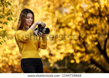 beautiful smiling woman photographer with camera takes pictures in park in autumn. copy space