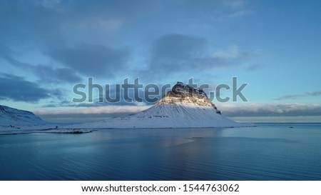 Mount Kirkufel at dawn in white snow is illuminated by morning sun on winter day in Iceland. calm sea around, blue sky, white clouds