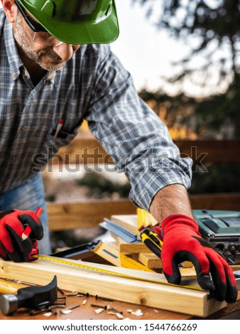 Adult carpenter craftsman wearing helmet and protective gloves, with the meter takes the measure on a wooden table. Construction industry, housework do it yourself. Stock photography.