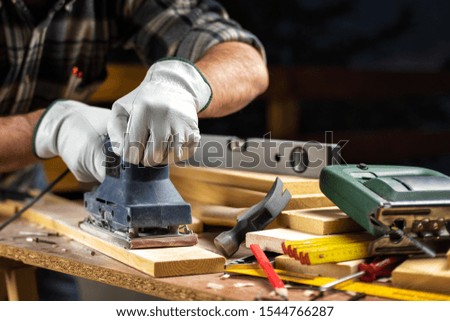 Adult carpenter craftsman wears protective leather gloves, with the electric sander smoothes a wooden table. Construction industry, housework do it yourself. Safety at work.