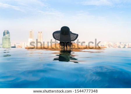 Young woman in a roof top swimming pool, infinity pool with beautiful city view. Vacation in Singapore.