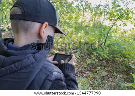 A child plays with the phone alone with nature, a problem of the modern young generation in the twenty-first century. The boy enthusiastically uses the gadget.