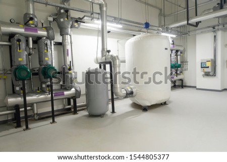 Piping inside industrial chiller plant room and buffer tank. Royalty-Free Stock Photo #1544805377