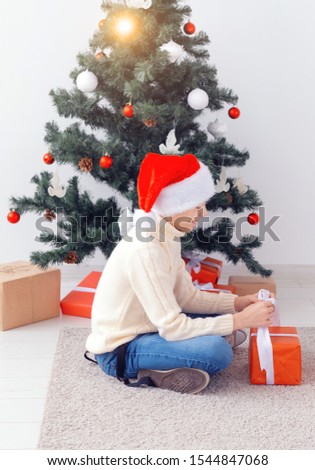 Holidays, christmas, childhood and people concept - smiling happy teen boy in santa hat opens gift box over christmas tree background