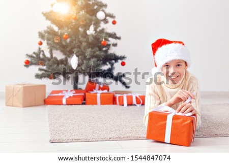 Holidays, christmas, childhood and people concept - smiling happy teen boy in santa hat with gift box over christmas tree background