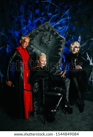 Gothic 3 friends in dark costumes with make up on a huge scary throne ready for Halloween party
