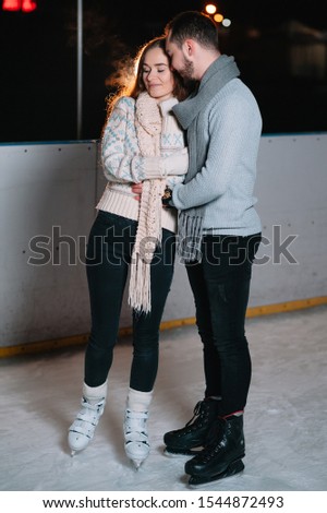 Winter skates, loving couple holding hands and rolling on rink. Illumination in background, night. Concept training.
