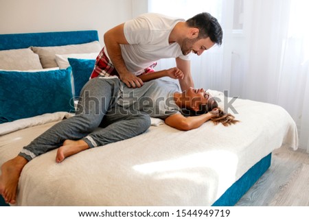 Beautiful loving couple kissing in bed. Loving and hugged couple on the bed in the room. Passionate love. Happy young couple hugging and smiling while lying on the bed in a bedroom at home.