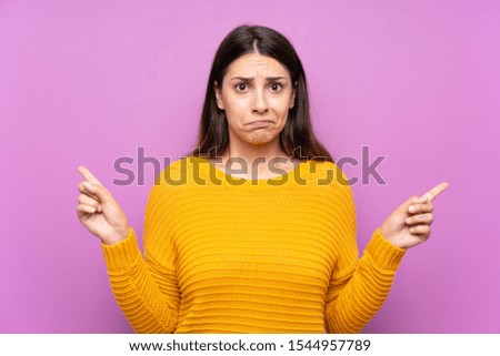 Young woman over isolated purple background pointing to the laterals having doubts