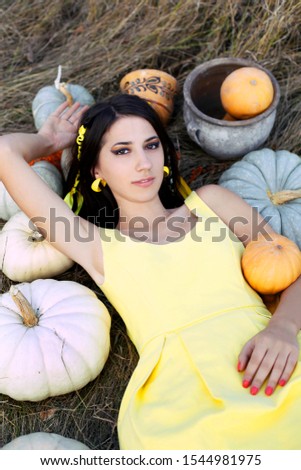 Attractive girl in yellow dress lie in the grass with pumpkins. Portrait of glamour girl with pumpkin