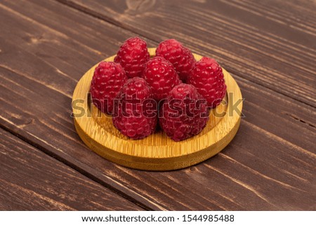 Group of seven whole fresh red raspberry on bamboo coaster on brown wood