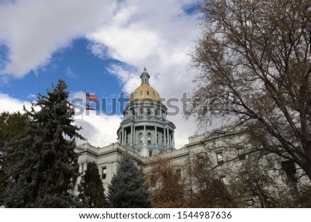 View of dome of Colorado State Capitol in Denver. American and Colorado flags waving in wind in front of the dome.