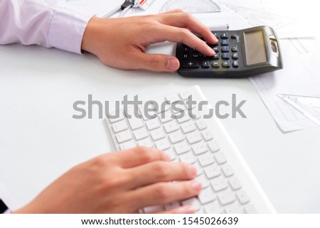 business hand working with finances about cost and calculator and laptop with tablet on withe desk at office warm colours sun light