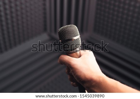 golden microphone in hand, gray background with acoustic foam in studio