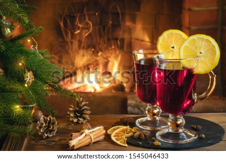 Christmas composition - two glasses with mulled wine on a wooden table near a Christmas tree opposite a burning fireplace