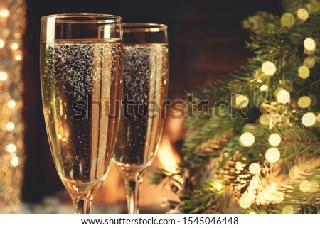 Christmas composition - Two glasses with champagne on a wooden table near a Christmas tree in a room with a burning fireplace