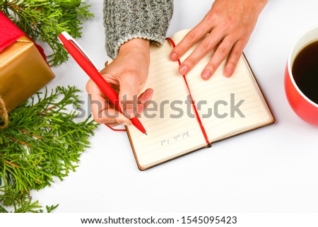 Writes wishes with a coffee mug. Dreams of goals plans make a list for writing new year christmas concept in notebook. Woman hand on a background with fir branches New Year winter holiday Christmas