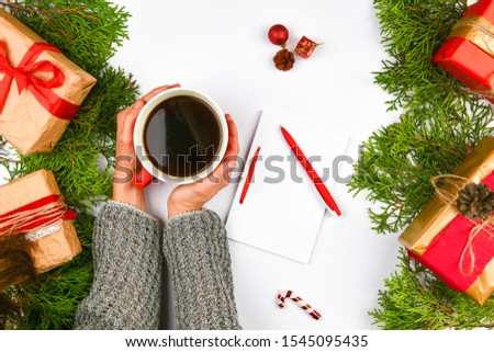 Hands holding a coffee mug on a Christmas background. View from above. Female hands holding coffee cup. Christmas gift boxes and snow fir tree above wooden table. Top view with copy space 
