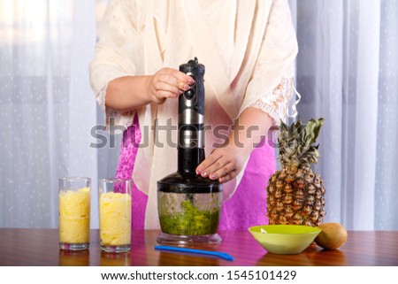 Woman crushes in a blender kiwi to mash.