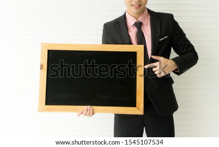 The close up of a young businessman smiling, holding and pointing at the blackboard with the white background and copy space for advertisement, marketing, and communication