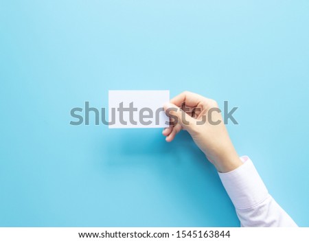 woman hand holding blank business name card paper isolated on blue background with copy space.
