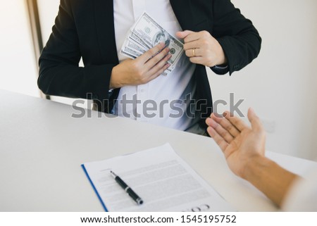 Businessman putting stack of money bills in his suit coat pocket.
