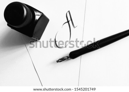 Sheets of white paper with handwritten letter A, next to a pen and a bottle of ink. The concept of learning calligraphy, letters. Minimalism, place for text.