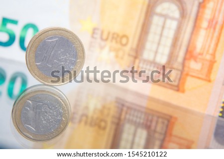 Macro photo of a coin in 1 euro on a blurred background banknote in 50 euro. Reflection of the coin on the glass table. Very small depth of field.