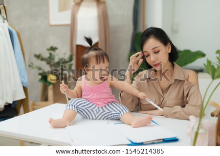 My mommy is a real expert! Little baby girl looking at camera while sitting on office desk with her mother in office