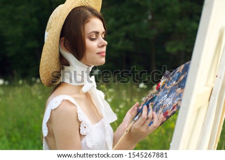 young woman outdoors an easel with a white canvas draws